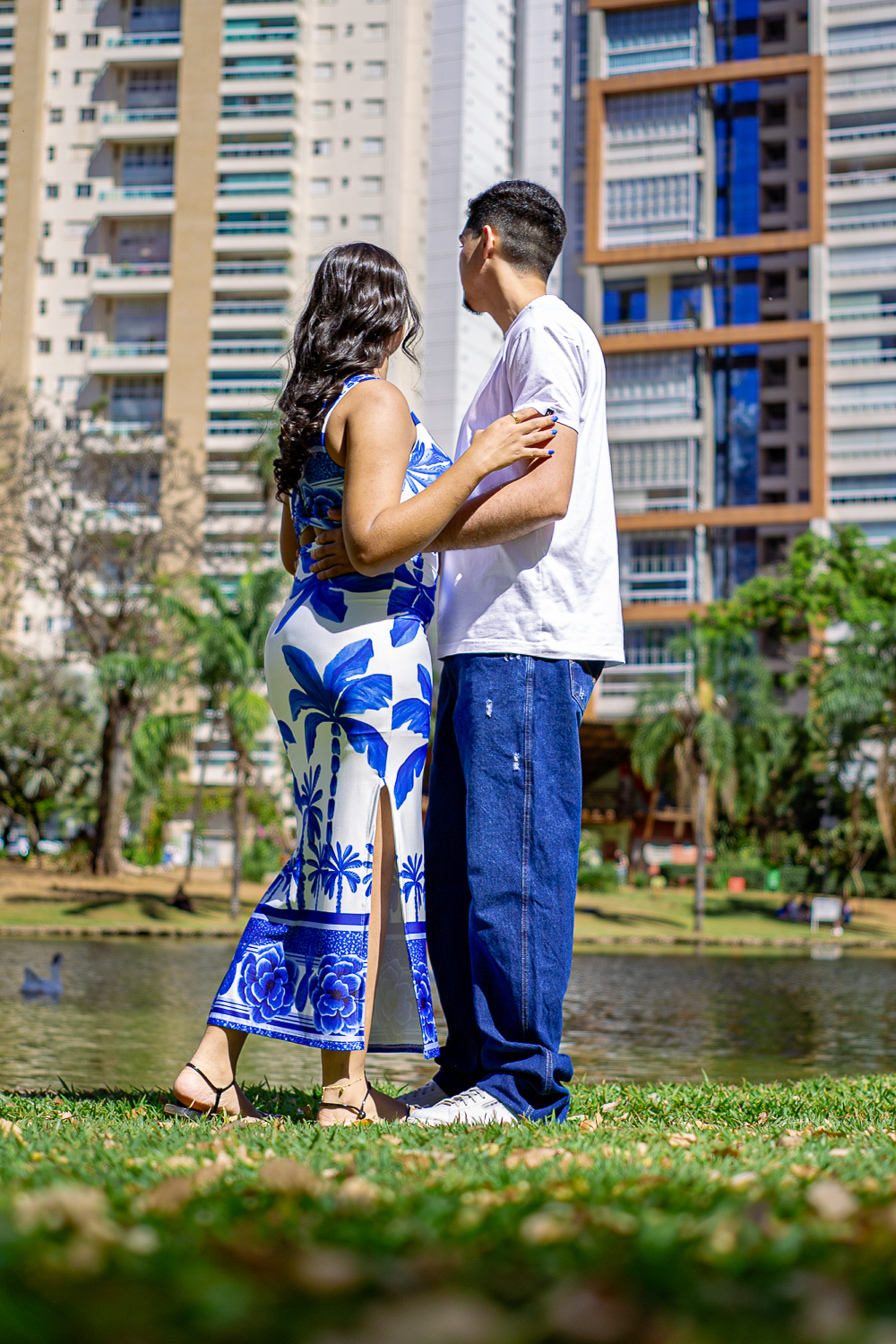 O casal de mãos dadas à beira do lago com prédios ao fundo